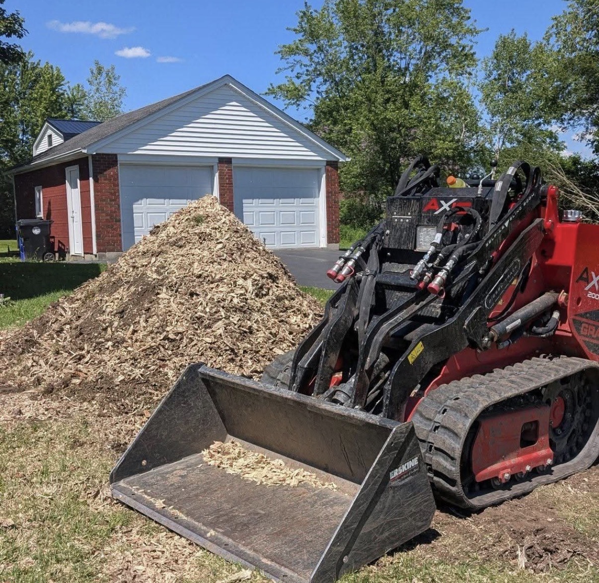 Skid loader beside a large pile of wood chips from a ground-out stump